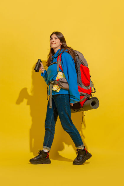 旅行黄色摄影棚墙上 一个带着包和望远镜的快乐的年轻旅游女孩的画像光明欢呼微笑