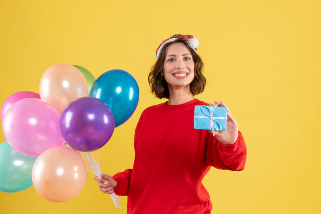 派对正面图年轻女子手持气球和小礼物在黄色圣诞假期新年情感色彩的女人正面气球颜色
