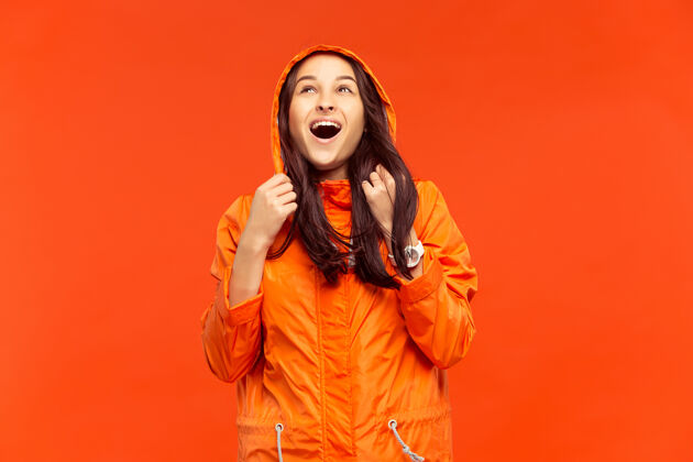 女性那个快乐微笑的小女孩穿着秋天的橘色夹克在摄影棚摆姿势 孤立在橘色的墙上衣服时尚肖像