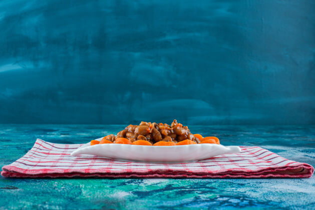 烘焙把切成片的胡萝卜和豆子放在茶巾上的盘子里 放在蓝色的背景上茶巾蔬菜豆类