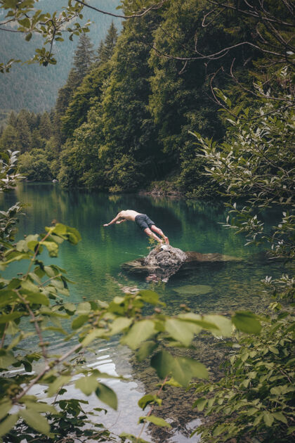 蔬菜赤裸上身的男人穿着黑色短裤准备在树旁的水上潜水湖泊土地冷杉