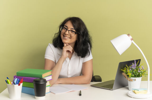眼镜年轻的笑容可掬的高加索女学生戴着眼镜坐在书桌旁 手里拿着学习用具 手放在下巴上 隔离在绿色空间和复印空间上下巴绿色漂亮