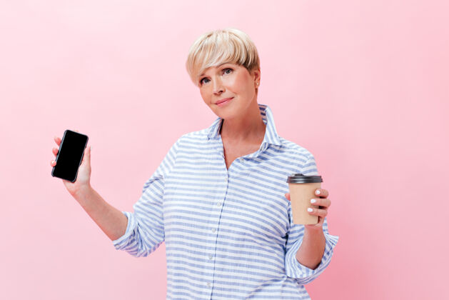 脸穿格子装的漂亮女士拿着茶杯和智能手机粉色背景数码女性