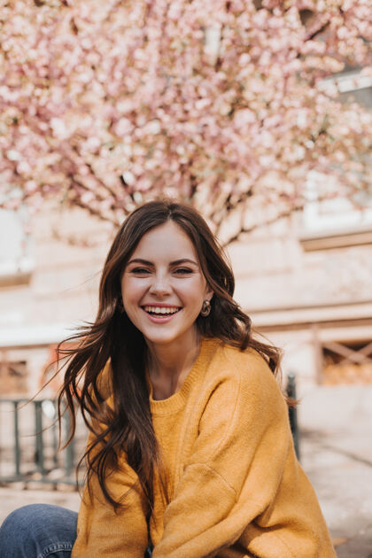 时尚的女人开朗的羊绒衫女孩在樱花盛开的背景下欢笑春天城市里穿着黄色连帽衫的女人的画像生活天健康