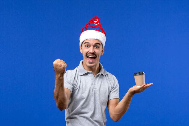 抱着正面图年轻男子拿着塑料咖啡杯在蓝色墙上感慨男子新年成人咖啡男人