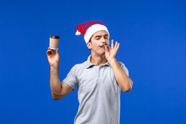 前面正面图年轻男性手持塑料咖啡杯在蓝色墙壁上男性新年假期塑料表演男性