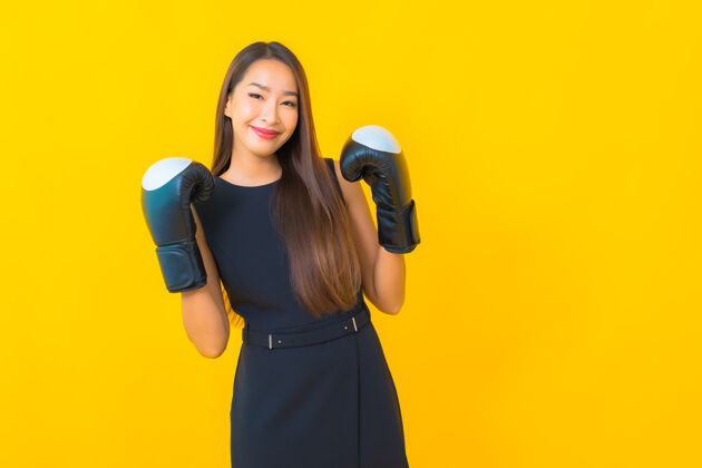 健身在黄色背景上画一个戴拳击手套的美丽的亚洲女商人行政人员手锻炼