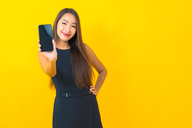 聪明一幅美丽的亚洲女商人的画像 黄色背景上有咖啡杯和智能手机年轻成人成功