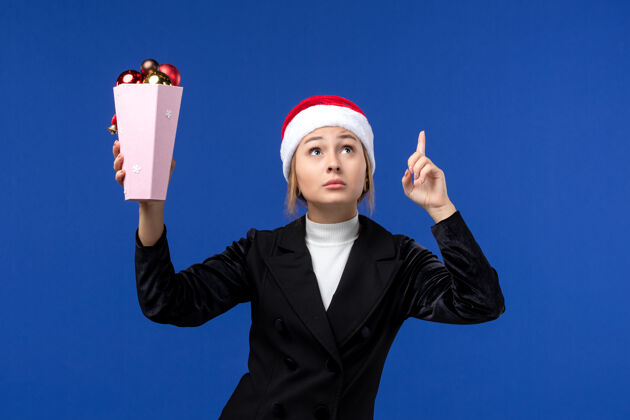 圣诞节正面图年轻女子拿着圣诞树玩具在蓝色墙上新年假期女子蓝色观点女人西装