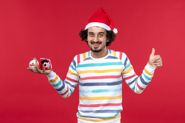 前面正面图：红墙红人新年假期手持塑料玩具的年轻人成人帽子微笑
