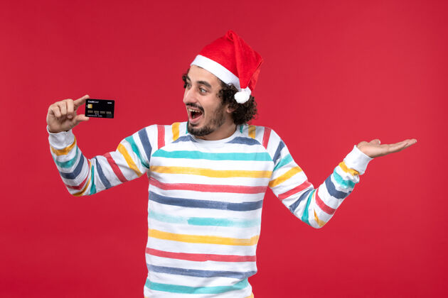 看面图年轻男子手持银行卡在红墙上感慨红男节日男性银行圣诞节