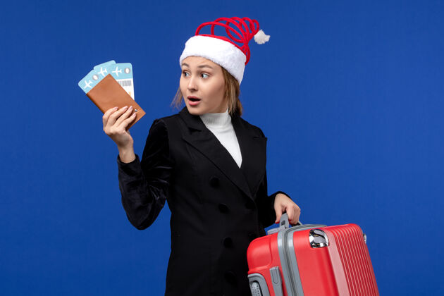 年轻的女性正面图：年轻女性拿着蓝色背景的女士度假包的票圣诞节人微笑