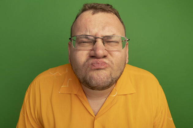 关上一个戴着眼镜 穿着橙色衬衫 眼睛紧闭的男人站在绿色的墙上不高兴站着伙计