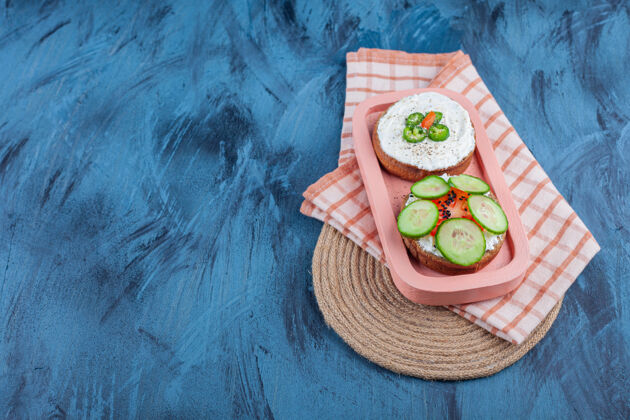 好吃的切好的蔬菜放在奶酪面包上 放在毛巾上 放在三角架上 放在蓝色的板上三叉戟黄瓜西红柿