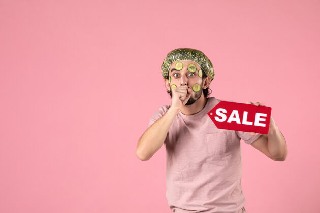 黄瓜正面图：年轻男性 脸上戴着面具 手持粉色背景的销售铭牌面部身体脸