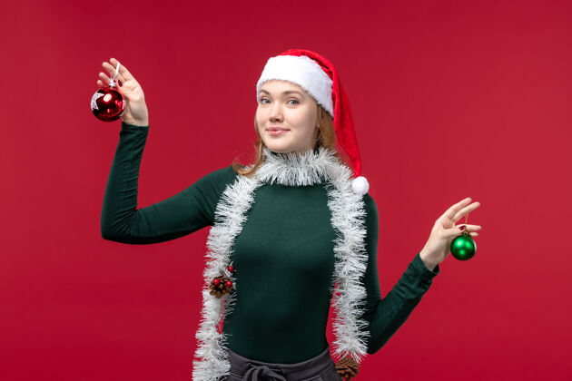 帽子正面图红色背景上手持圣诞树玩具的年轻女性人物红色服装