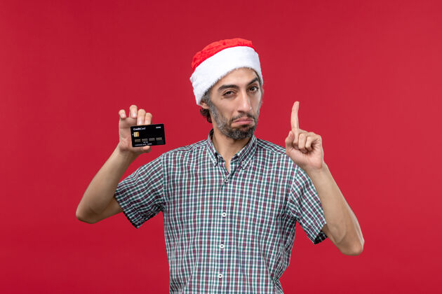 人正面图年轻男子手持红色背景的黑色银行卡钱圣诞节卡片