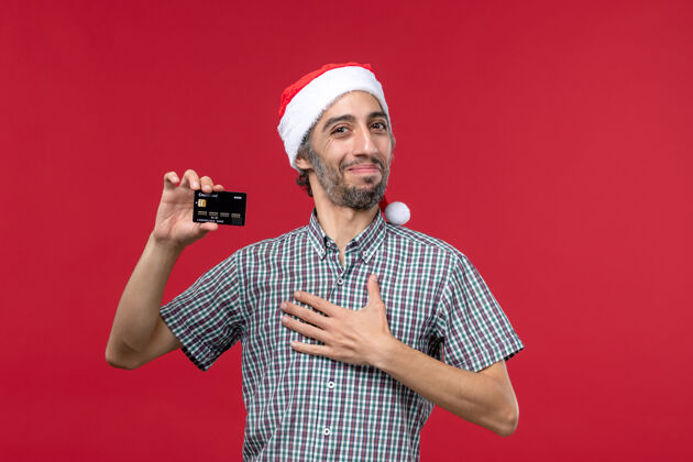 圣诞节正面图年轻男子手持红色背景的黑色银行卡红色成人男人
