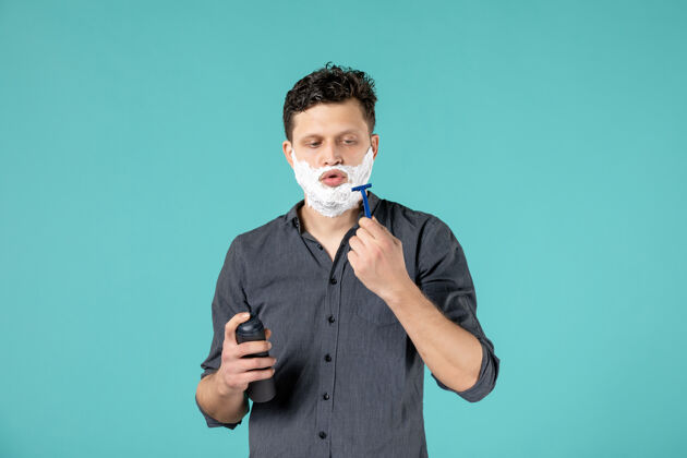 洗澡正面图：年轻男性 脸上有泡沫 准备在蓝色背景上刮胡子前面男性男人