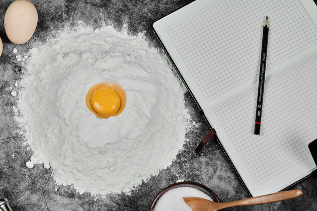 面粉面粉上的蛋黄 石头桌上的笔记本和铅笔准备面包房顶视图
