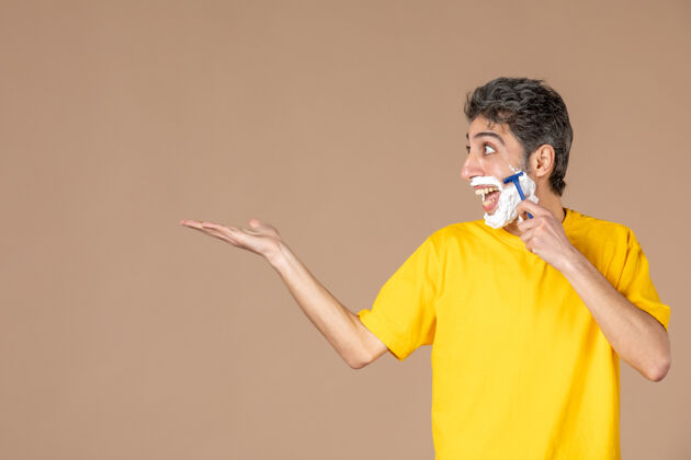 视图正面图：年轻男性在粉色背景上剃着泡沫脸身体护理面部肖像