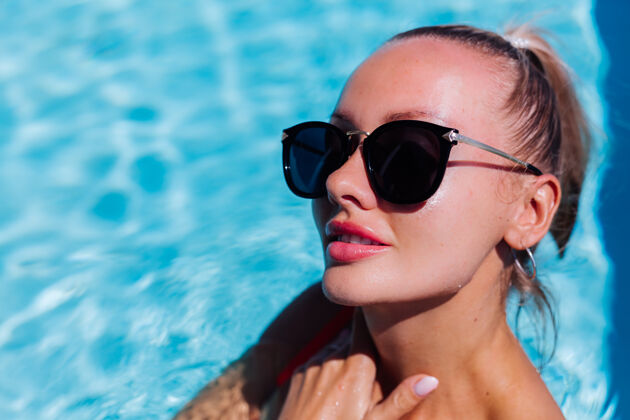 华丽阳光明媚的日子里 蓝色游泳池里 戴着太阳镜 皮肤黝黑的平静快乐女人的画像发型女士风格