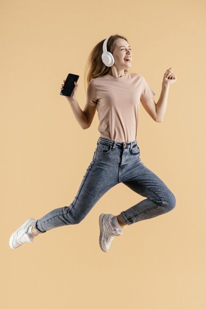 科技带着耳机和手机跳跃的年轻女性表达跳跃年轻