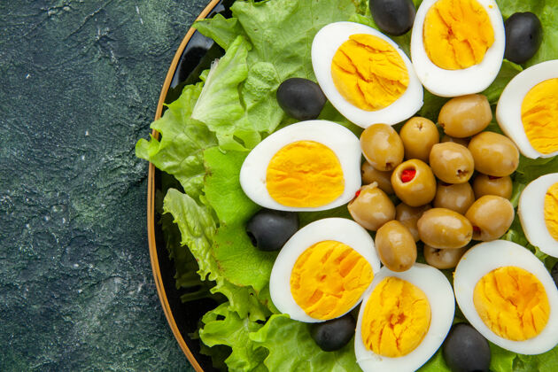 饮食顶部近距离查看煮熟切片鸡蛋与橄榄和绿色沙拉在黑暗的背景生菜绿色一餐
