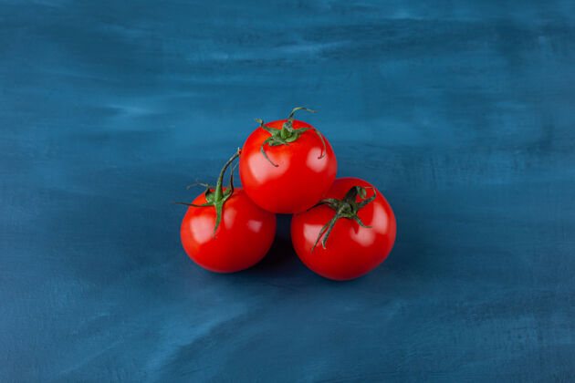 成熟三个红色的新鲜西红柿放在蓝色的表面上美味红蔬菜