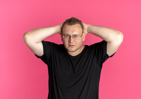 站一个戴眼镜的胖男人穿着黑色t恤 看起来很困惑 手放在头上 超过了粉色黑色手粉色