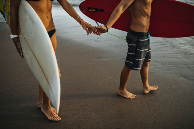 女性穿着沙滩装的男人和女人在潮湿的沙滩上行走 拿着冲浪板感情关系男人