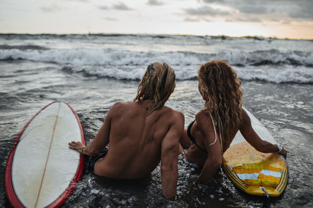 情侣男人和女人坐在沙滩上冲浪板海洋女人冲浪板