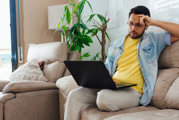 白种人一位英俊的西班牙裔男子坐在沙发上使用笔记本电脑的照片年轻年轻室内