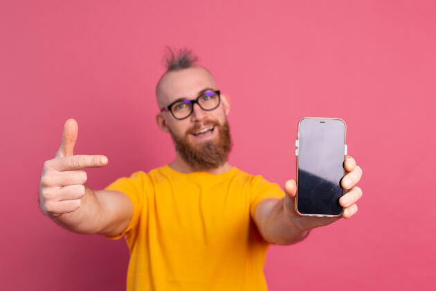 惊喜嘿 新来的东西快乐的欧洲胡子家伙指着他的手机 黑色的空白屏幕上的粉红色兴奋电话抱着
