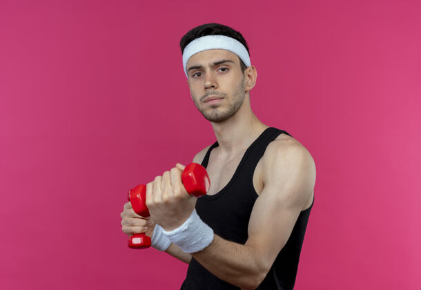 粉色年轻的运动型男子戴着头巾 戴着哑铃 紧张而自信地在粉色的头上锻炼运动年轻自信
