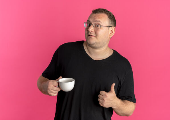 粉色戴眼镜的超重男子身穿黑色t恤 手持咖啡杯 竖起大拇指 对粉色微笑杯子男士超重