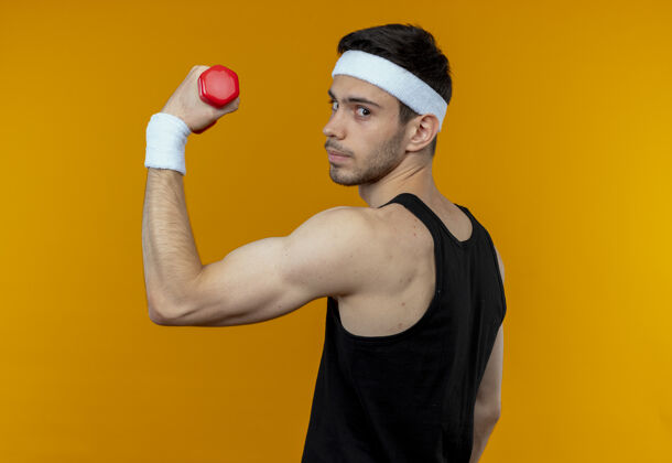 抱年轻的运动型男子戴着头巾举着哑铃 站在橙色的墙上做着练习 看上去很自信男人哑铃站