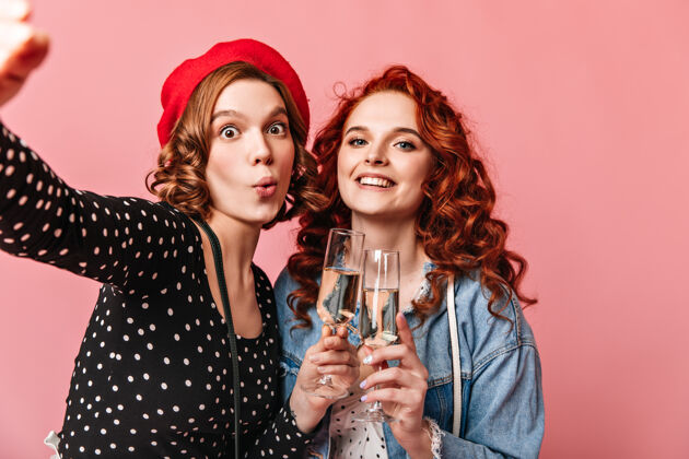 一起有趣的女孩拿着香槟自拍两个最好的朋友在享受活动 拿着粉红色背景的酒杯友谊粉色背景女性