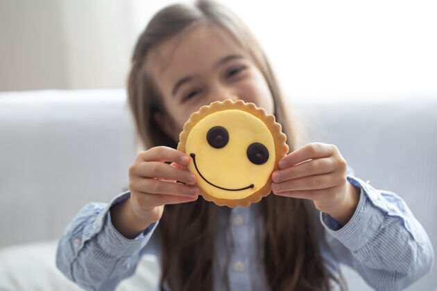 饼干一个穿着衬衫的小学女生拿着一块亮黄色的笑脸饼干 背景模糊笑脸姜饼明亮