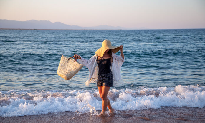 海岸一个戴着大帽子和柳条袋的女孩沿着海边散步暑假概念女孩帽子夏天