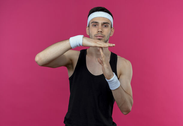 站立戴着头巾的年轻运动型男子 严肃的脸上摆着超时手势 手放在粉色的上方年轻时间粉色
