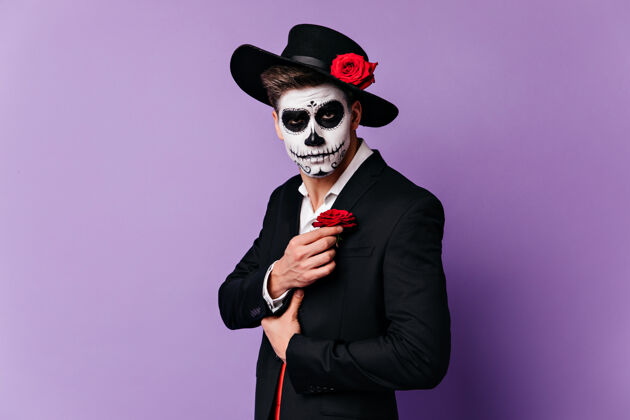 万圣节戴着黑帽子的僵尸男子在紫色背景上摆姿势室内拍摄的男模在庆祝万圣节的浓密睡衣中墨西哥嘉年华音乐家