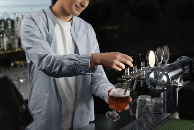 酒吧特写镜头：一个正在往杯子里倒啤酒的人享受酒精饮料