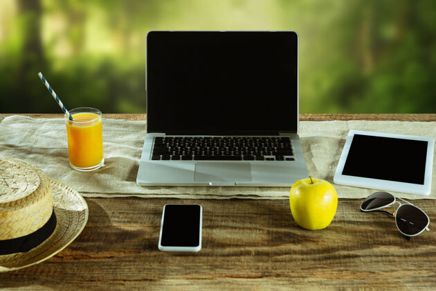 笔记本电脑户外木桌上摆放着笔记本电脑和智能手机的空白屏幕 墙上挂着自然的水果和新鲜的果汁创意工作场所 商业 自由职业者的概念复制空间窗户屏幕办公室