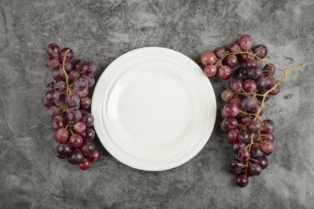 成熟白色的盘子和红色美味的葡萄放在大理石桌上浆果集群美味
