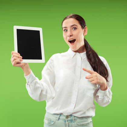 快乐一个自信的休闲女孩的肖像 展示了隔离在绿墙上的笔记本电脑的空白屏幕技术女性欢呼