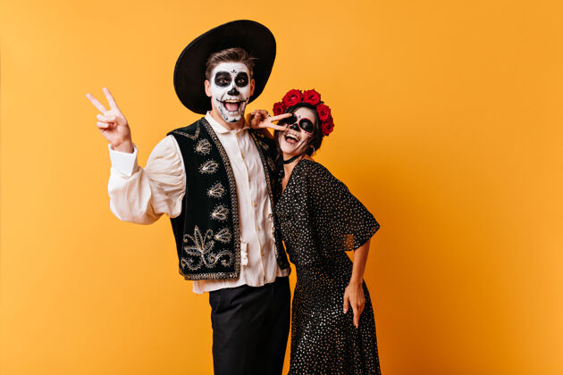 万圣节情绪激动的黑发男孩和他的女朋友在墨西哥服装显示和平标志的乐趣化妆恐怖死亡日