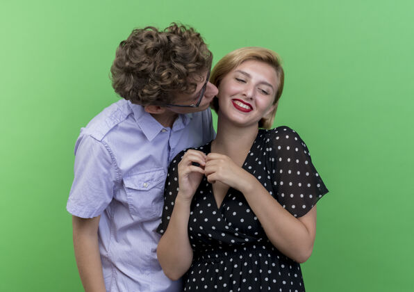 亲吻年轻漂亮的夫妇幸福的男人亲吻他心爱的女友站在绿色的墙站立年轻亲爱的