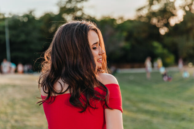 青春可爱的女人 优雅的发型 在公园里摆姿势快乐的白人黑发女孩 穿着红裙子 看着草地优雅幸福草
