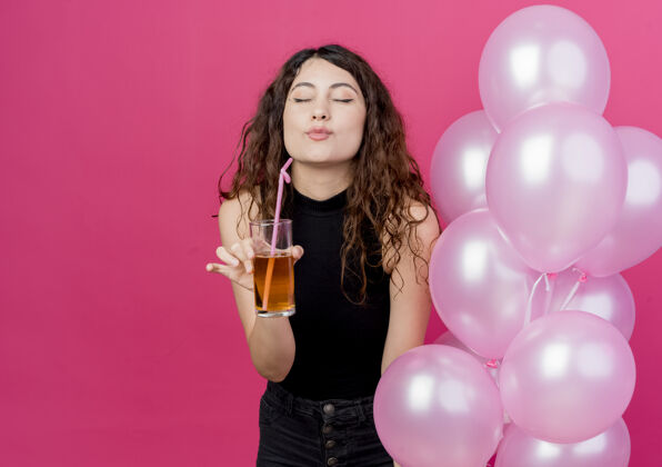 束一位年轻漂亮的女士 卷发 手持一束气球和鸡尾酒 快乐而积极地站在粉红色的墙上女人积极气球